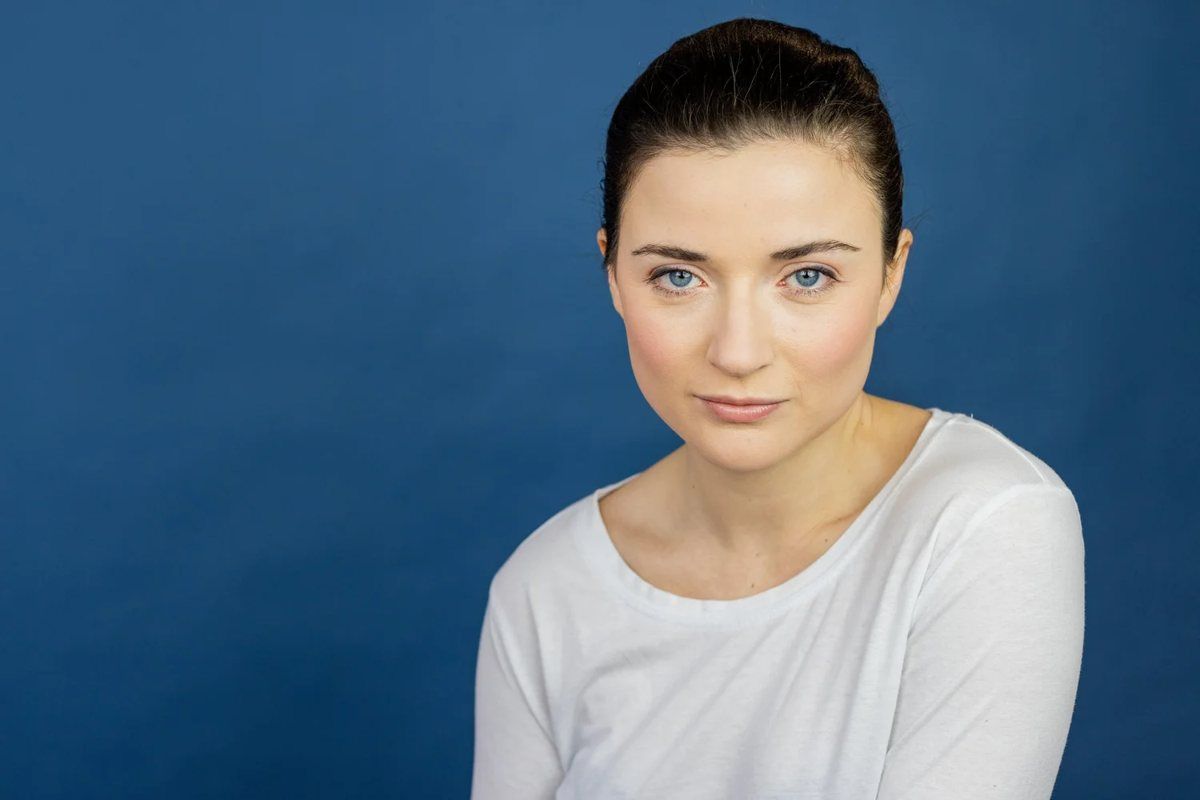 Studio headshot of a woman in a white top on a navy backdrop